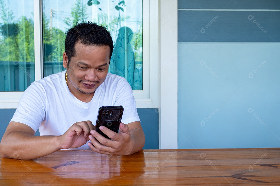 Homem asiático vestindo camisa branca usando o telefone em uma mesa de madeira.