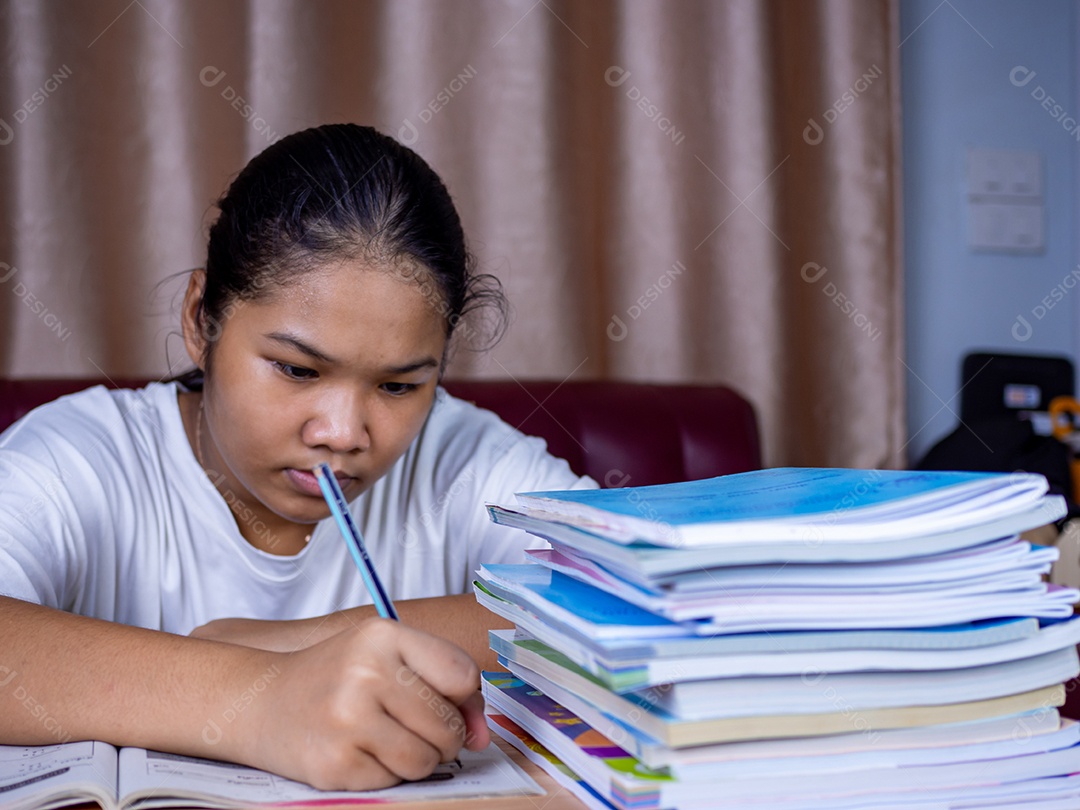 Menina fazendo lição de casa em uma mesa de madeira e havia uma pilha.