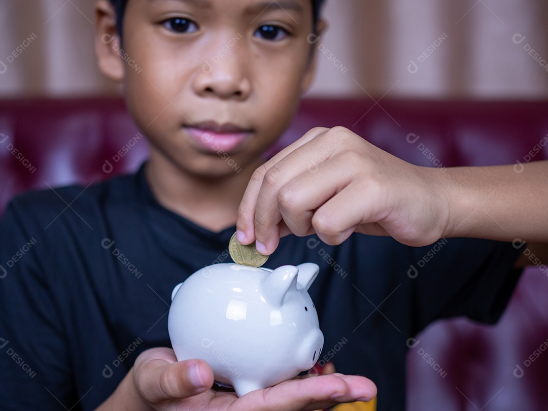 Menino economizando dinheiro em um cofrinho de porco branco. Conceito de economia. Poupar para o futuro.