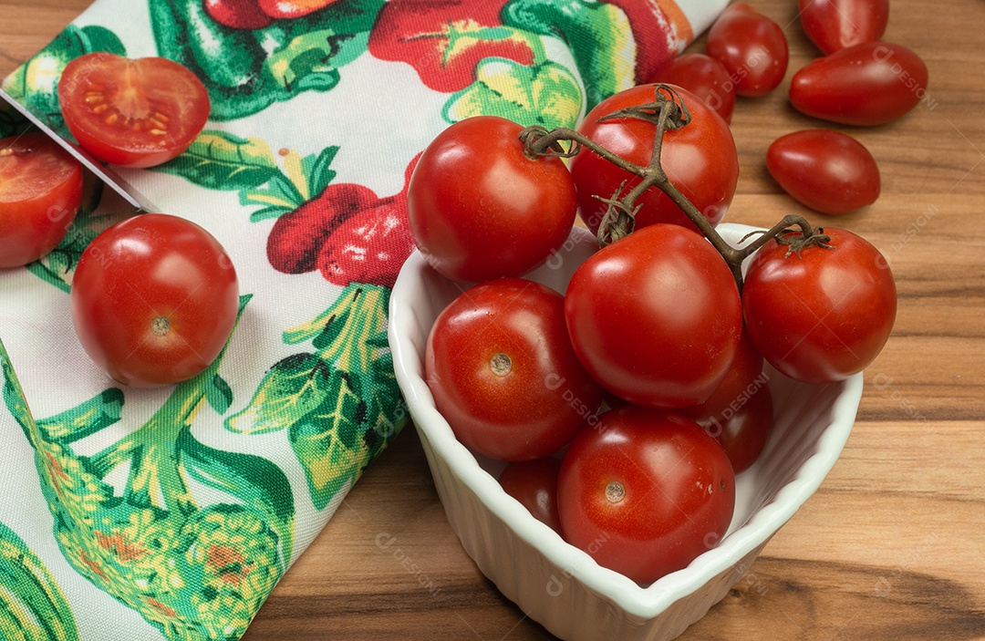 Dois tipos de tomate dentro de uma tigela branca sobre uma mesa de madeira com fundo preto