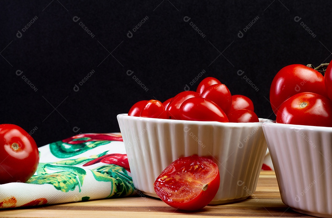 Dois tipos de tomate dentro de uma tigela branca sobre uma mesa de madeira com fundo preto