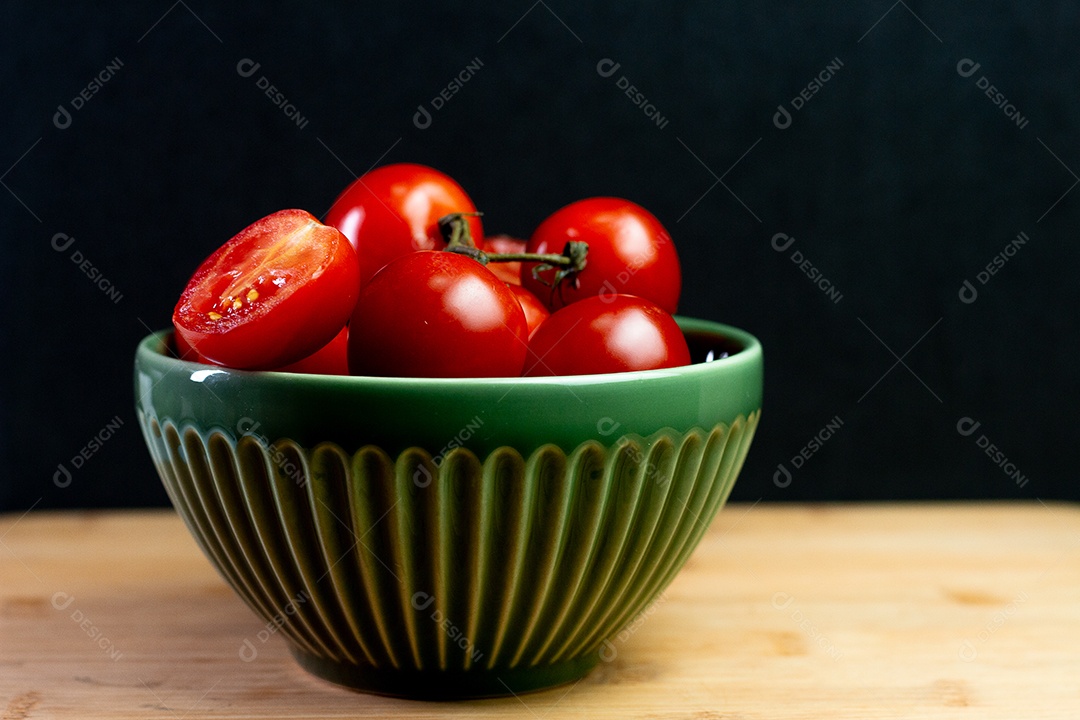 Tomates dentro de uma tigela verde sobre uma mesa de madeira com costas pretas