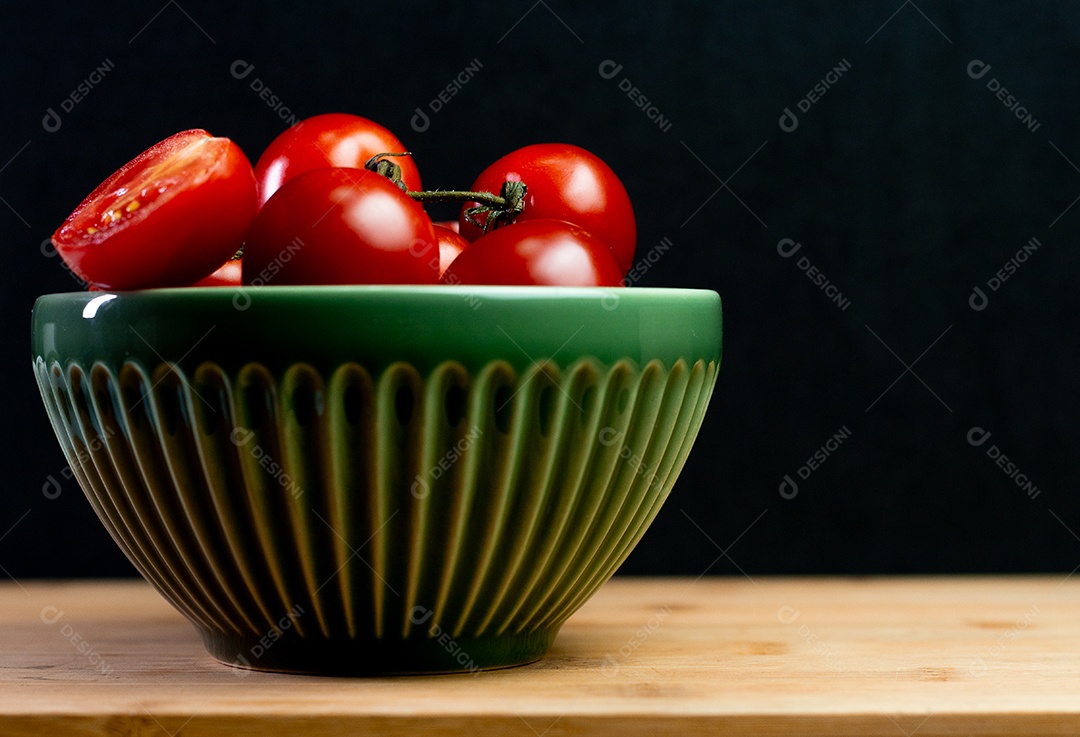 Tomates dentro de uma tigela verde sobre uma mesa de madeira com costas pretas