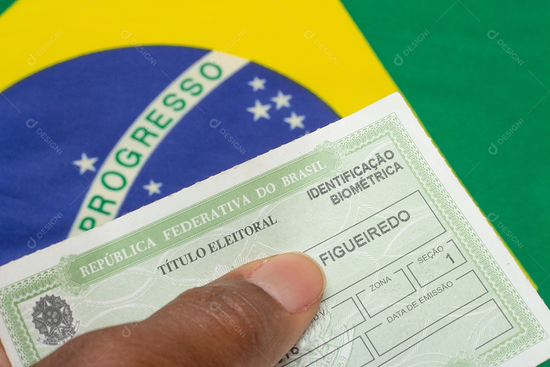 mão segurando o documento eleitoral brasileiro perto da bandeira brasileira