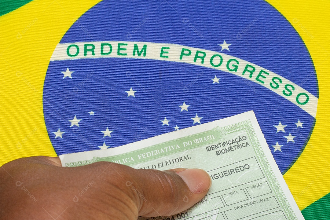 mão segurando o documento eleitoral brasileiro perto da bandeira brasileira