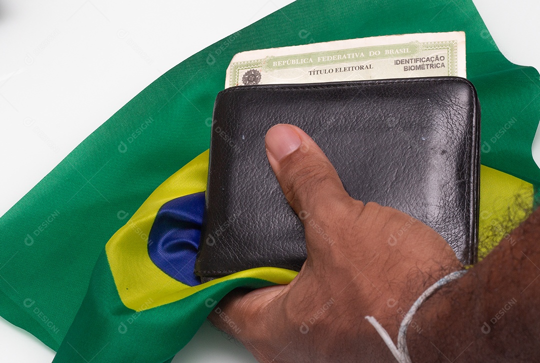 Homem segurando uma carteira com título de eleitor brasileiro sob a bandeira brasileira