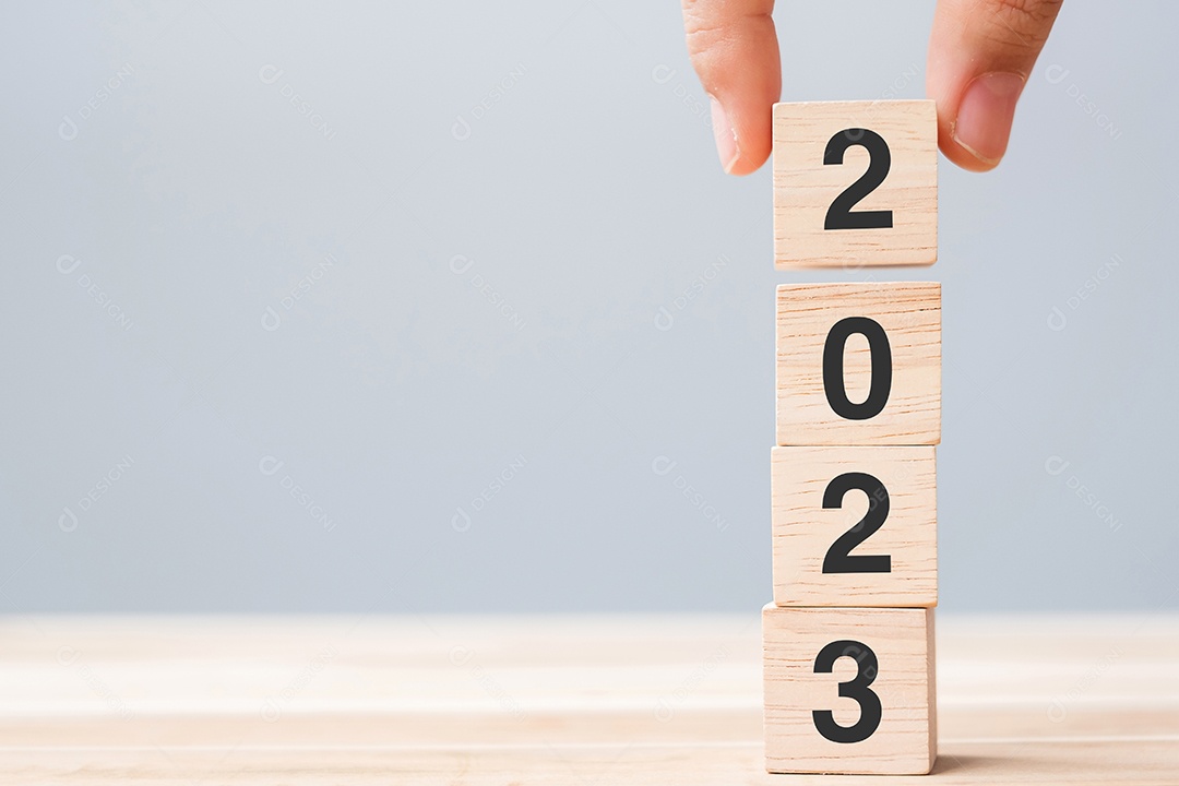 Mão segurando o bloco de cubo de madeira com texto 2023 no fundo da mesa.