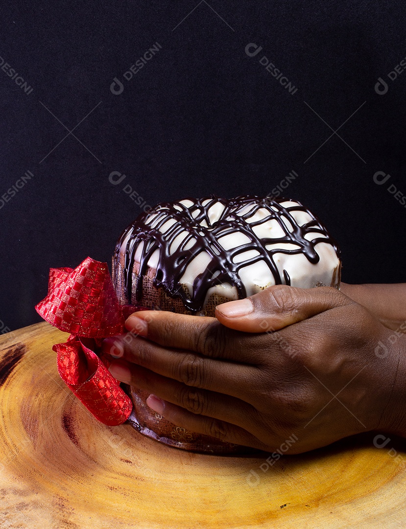 Mãos segurando um panetone em uma mesa de madeira com gravata vermelha