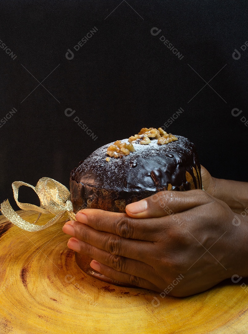 Mãos segurando um panetone em uma mesa de madeira com gravata vermelha