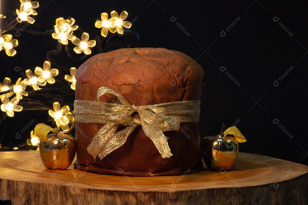 Panetone cercado por um pequeno presente dourado com fundo preto
