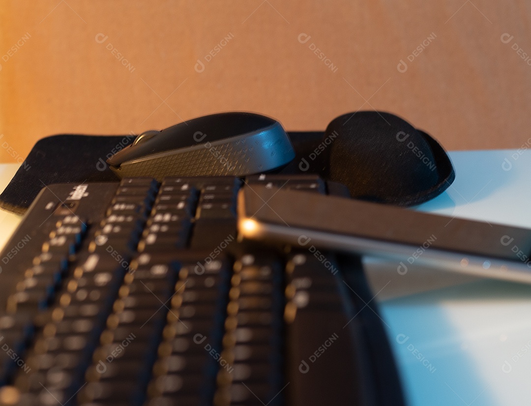 Mouse e celular em um teclado em uma mesa branca com uma luz quente