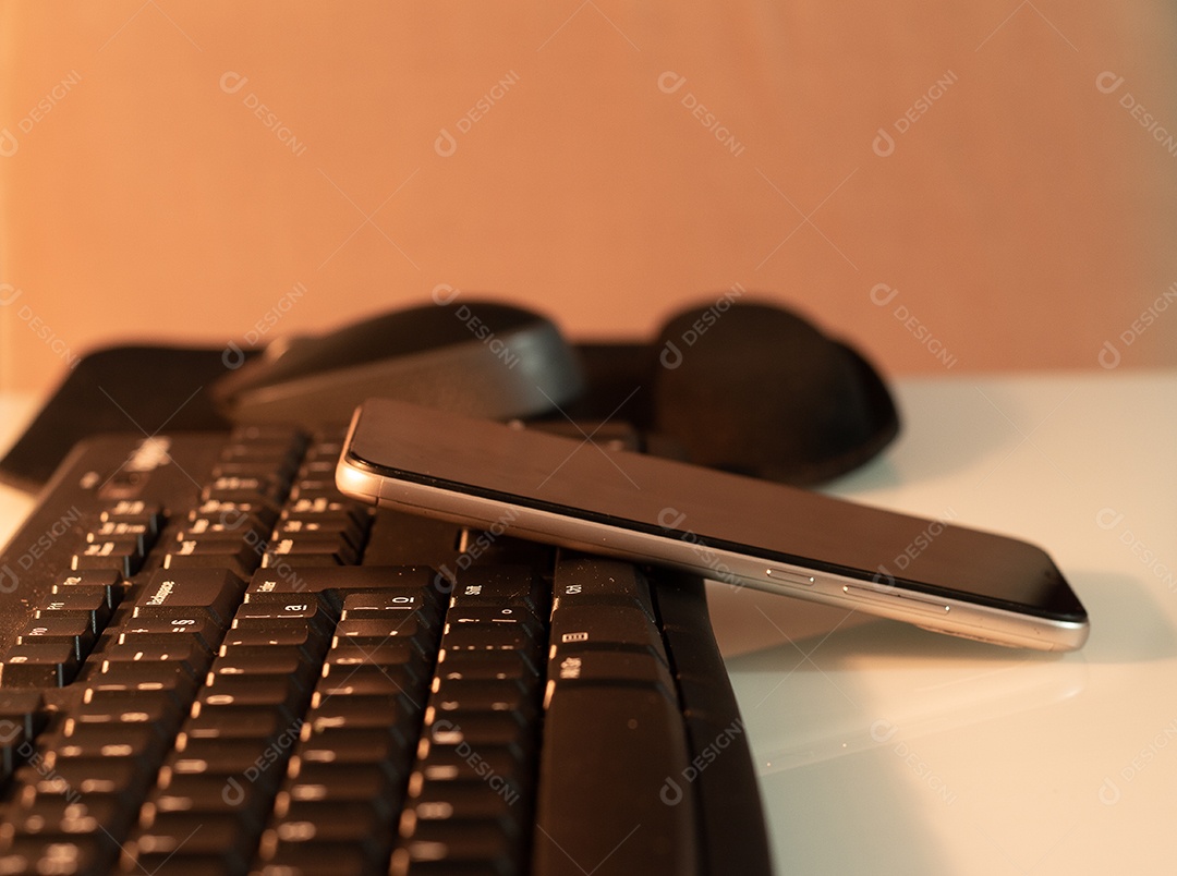 Mouse e celular em um teclado em uma mesa branca com uma luz quente