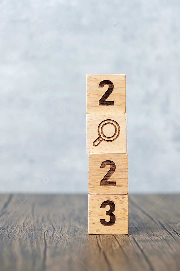 Mão segurando o bloco de cubo de madeira com texto 2023 no fundo da mesa.