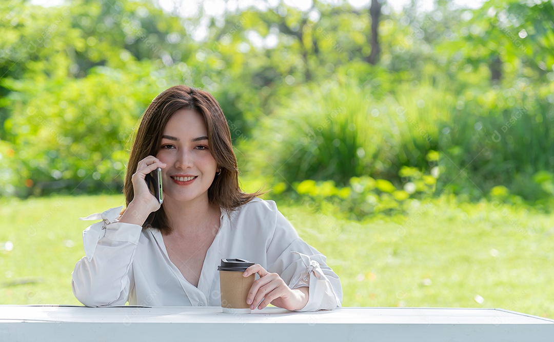 Linda mulher asiática usa telefone celular e feliz e segurando café