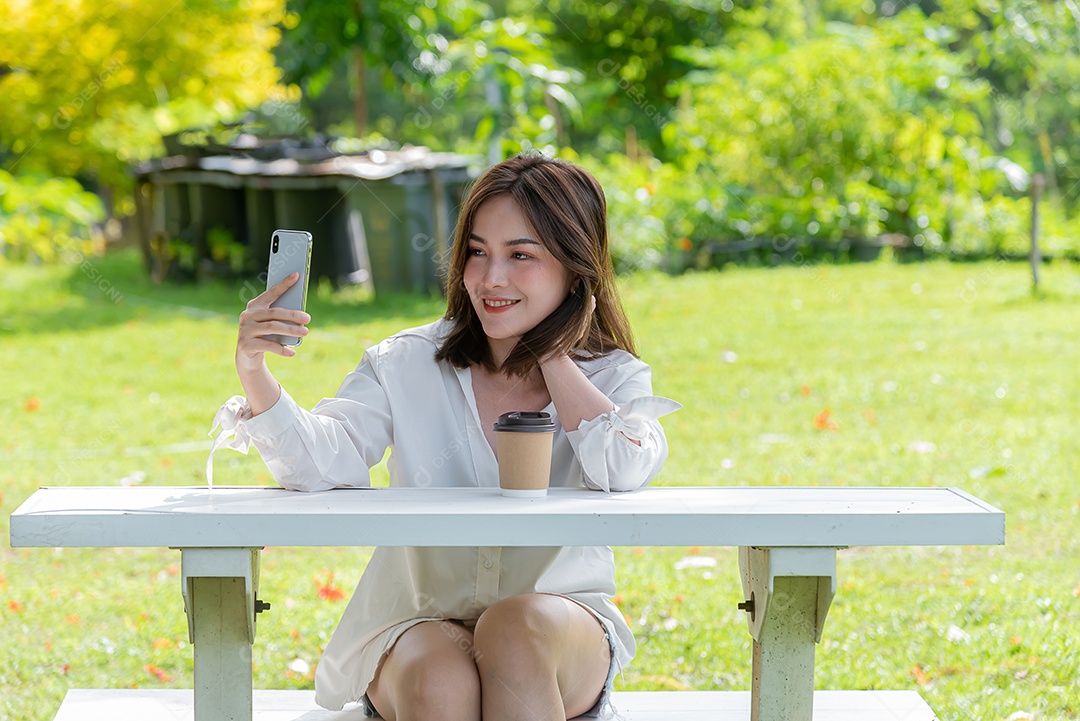 Linda mulher asiática usando smartphone tomando selfie no parque