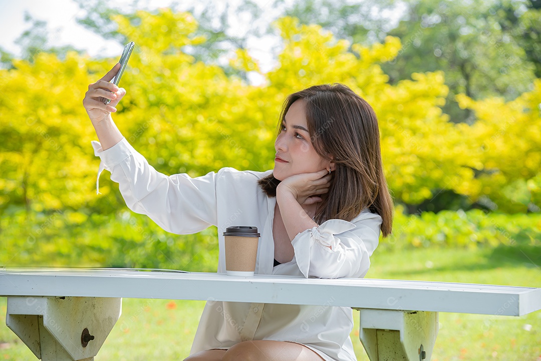 Linda mulher asiática usando smartphone tomando selfie no parque