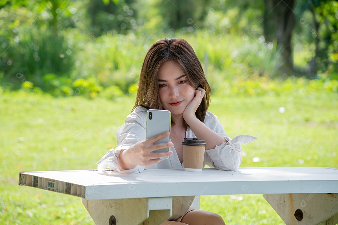 Linda mulher asiática usando smartphone tomando selfie no parque