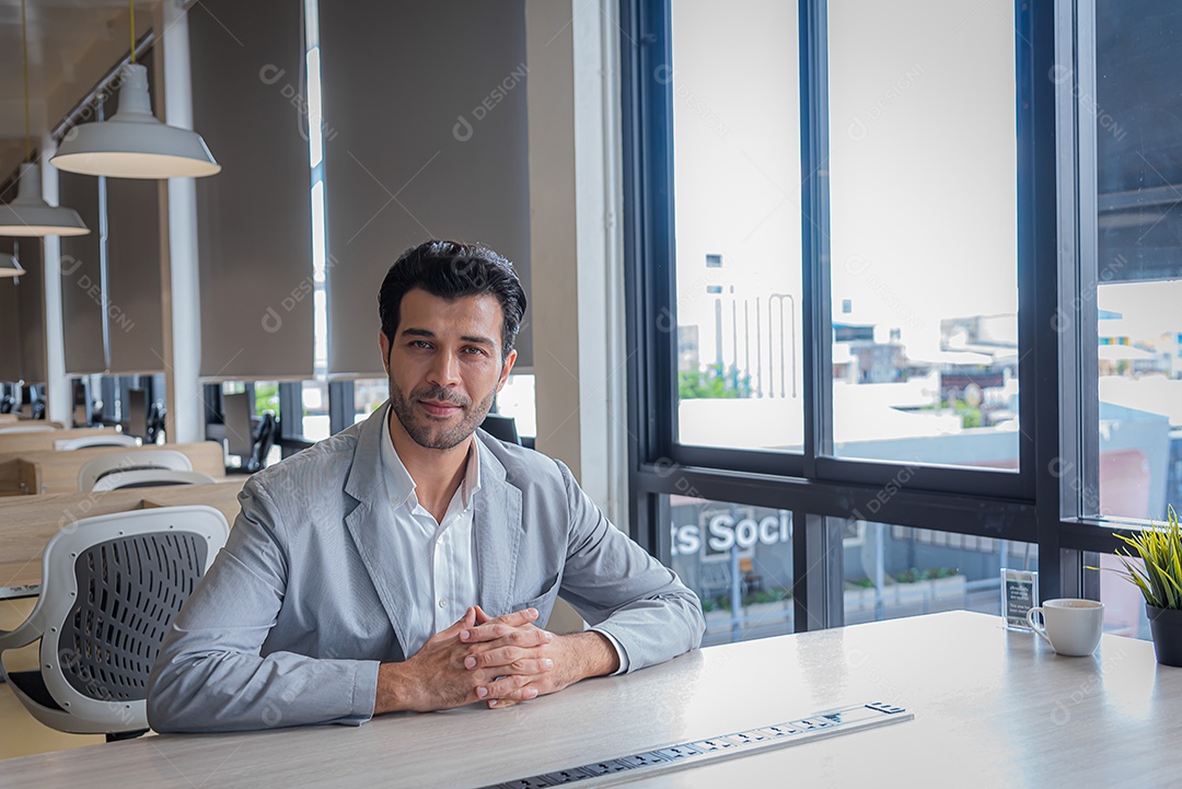 O homem de negócios senta-se no escritório moderno e olha para a câmera