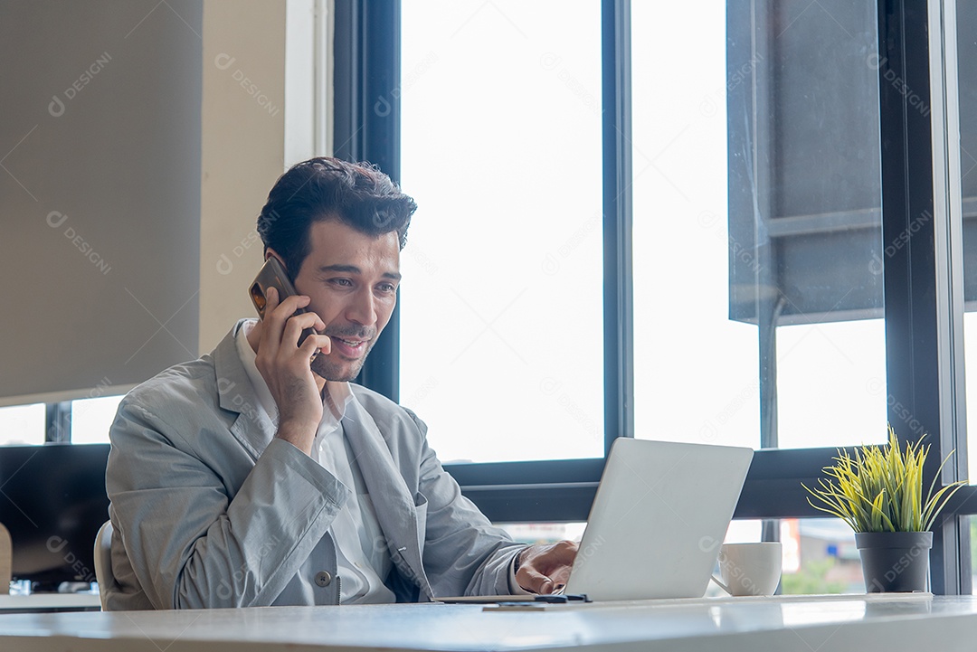 Homem de negócios trabalhando em seu laptop em um escritório e usa o celular