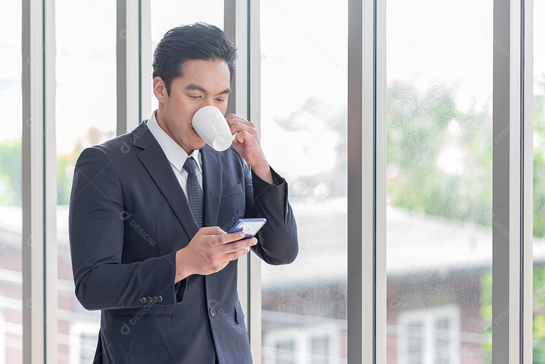 Homem de negócios asiático bebe café e usa telefone celular