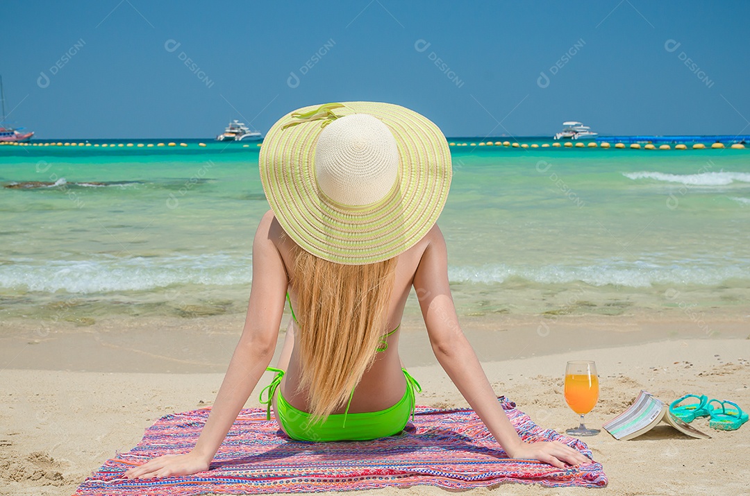 A mulher asiática veste um biquíni verde sentado na praia