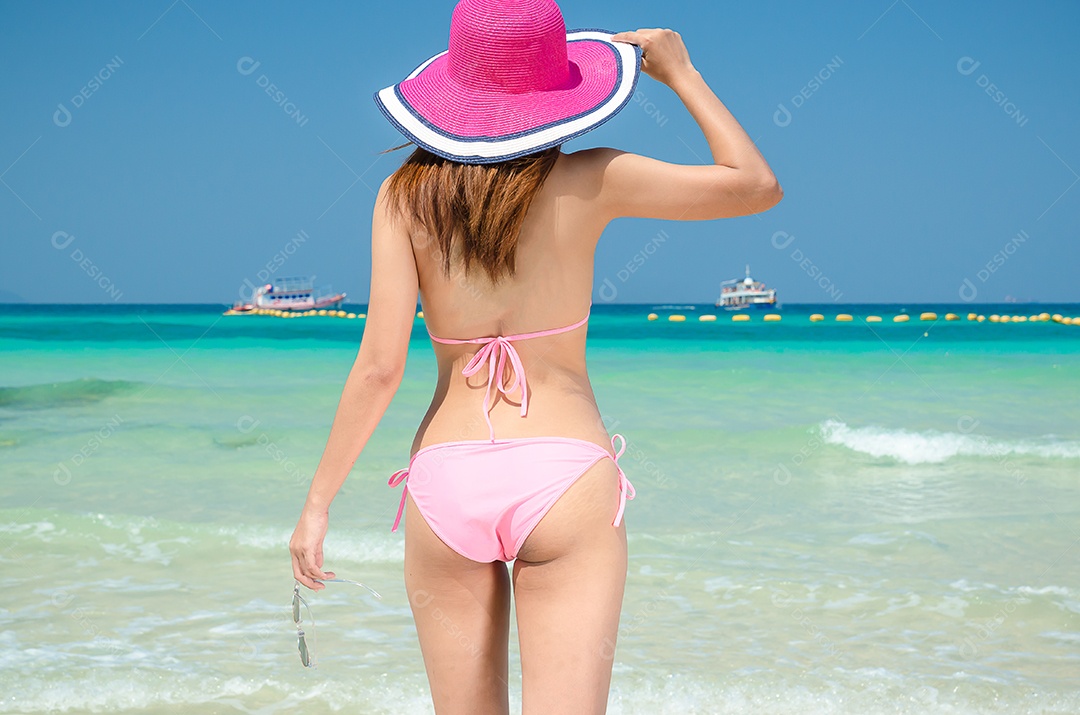 A mulher asiática veste um biquíni rosa na praia