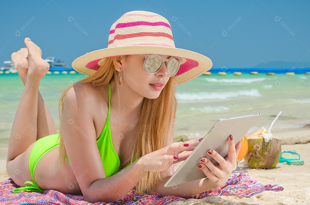 Mulher bonita dorme na praia usa chapéu e usa tablet