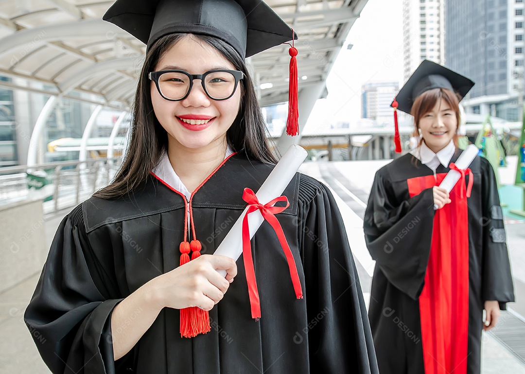 Dois estudantes universitários, mulheres asiáticas, usam vestidos, realizam a formatura