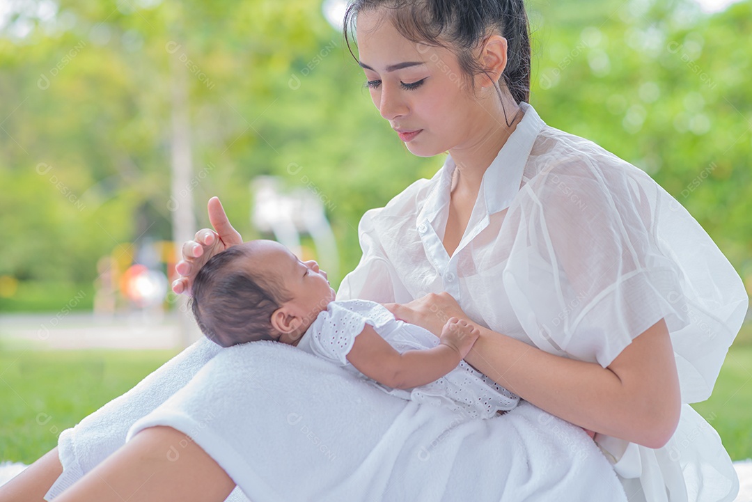 Mãe carrega e toca seu filho com ternura e carinho sentado no parque.