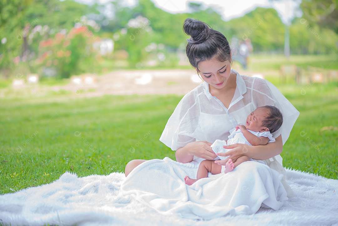 Mãe carrega e toca seu filho com ternura e carinho sentado no parque.