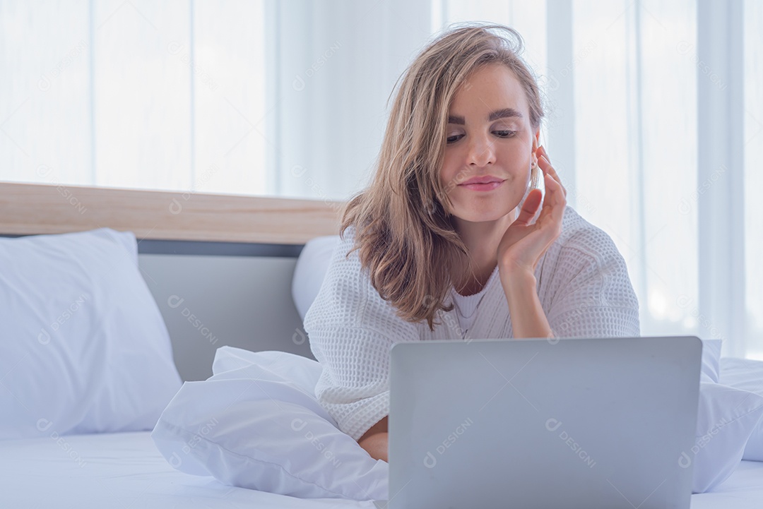 Mulher usando notebook de computador na cama olha rede social na internet.
