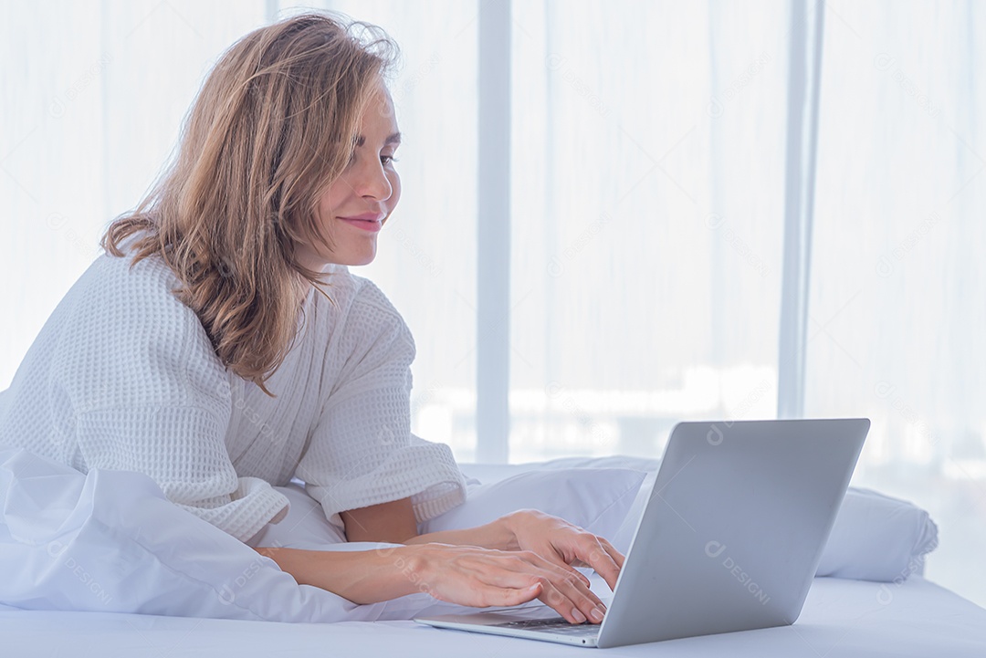 Mulher usa notebook de computador na cama olha rede social na internet.