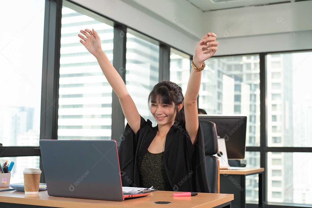 Mulher asiática de beleza levantando as duas mãos depois de terminar o trabalho feliz, sorrindo olhando a tela do laptop.