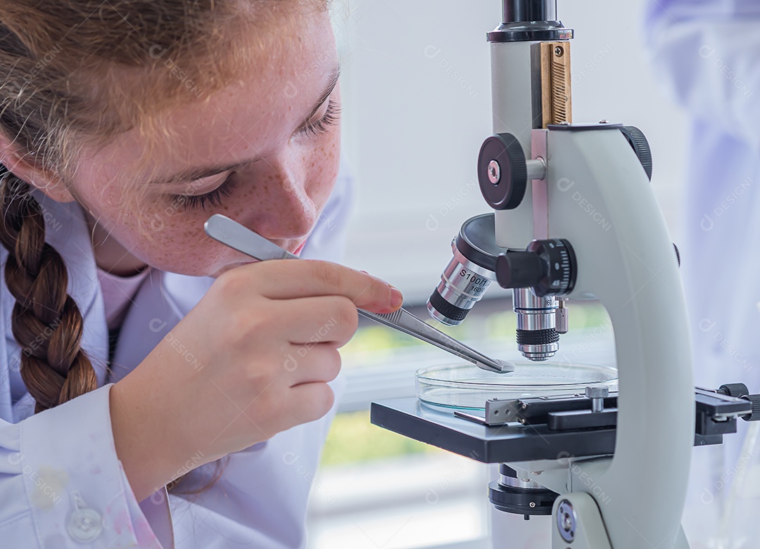 Mulher das crianças estuda assuntos científicos e usa o microscópio.