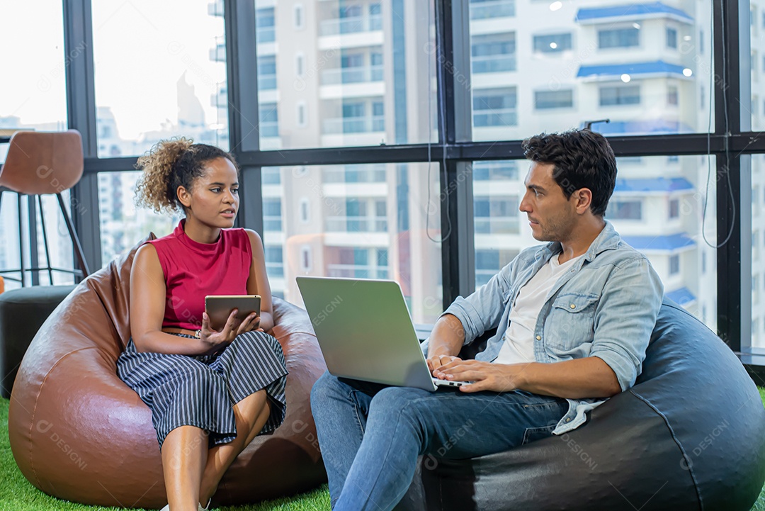 Jovem olha a câmera e a mulher africana usa o notebook no escritório moderno.