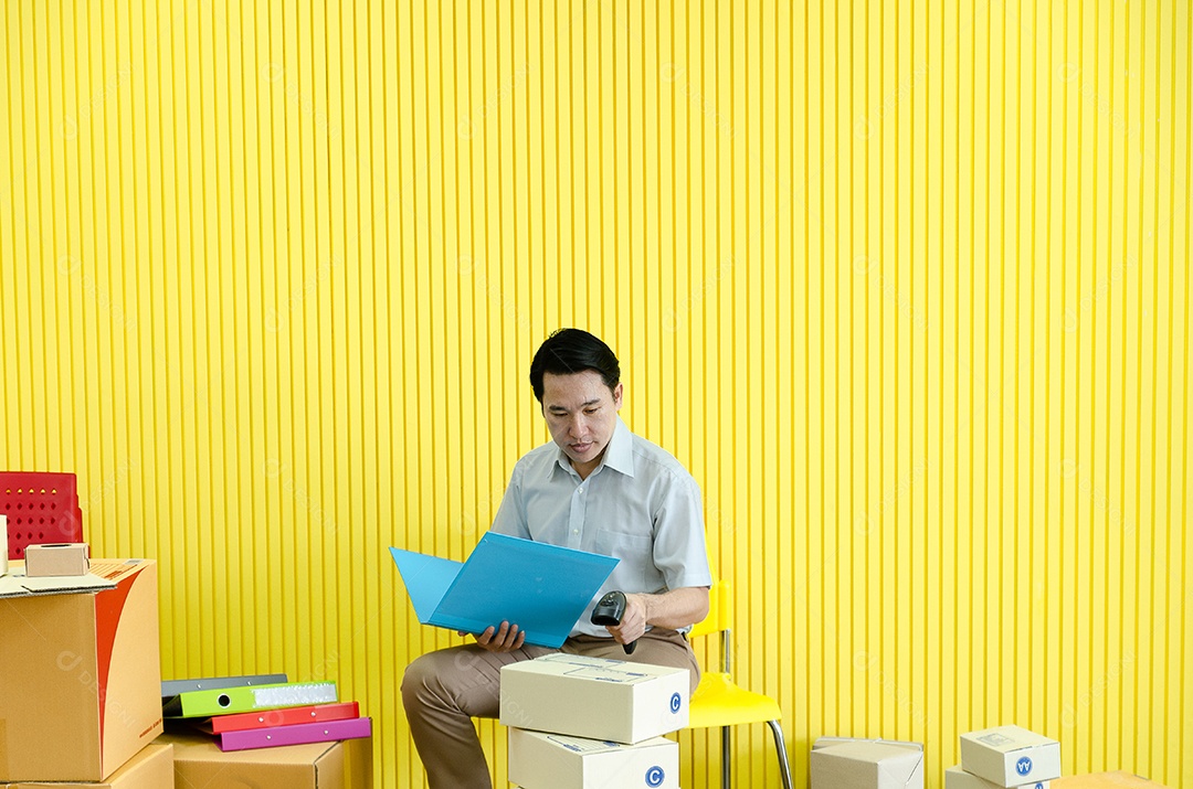 Pequeno empresário asiático feliz segurando dólar e preparando mercadorias para clientes, fundo amarelo.