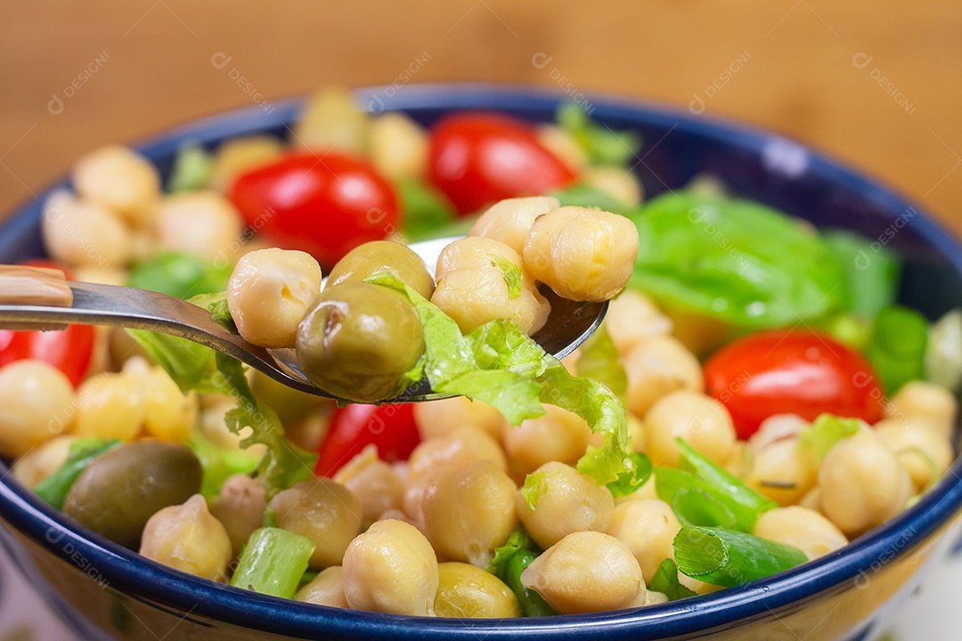Colher com grão de bico com folhas, azeitonas e tomates em uma tigela azul