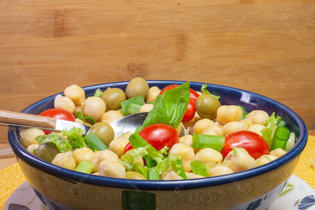 Colher com grão de bico com folhas, azeitonas e tomates em uma tigela azulc