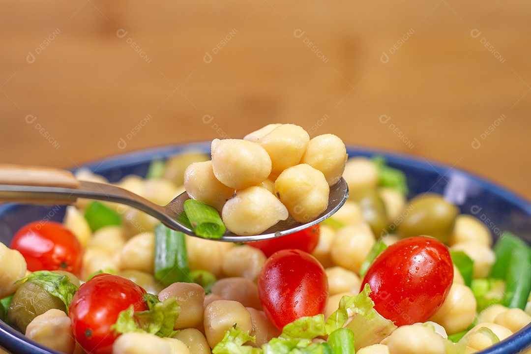 Colher com grão de bico com folhas, azeitonas e tomates em uma tigela azul
