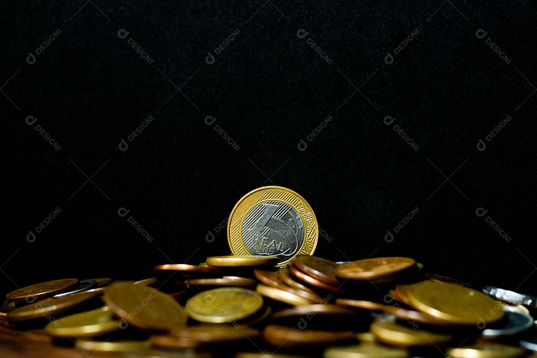 Moeda real brasileira cercada por moedas com fundo preto