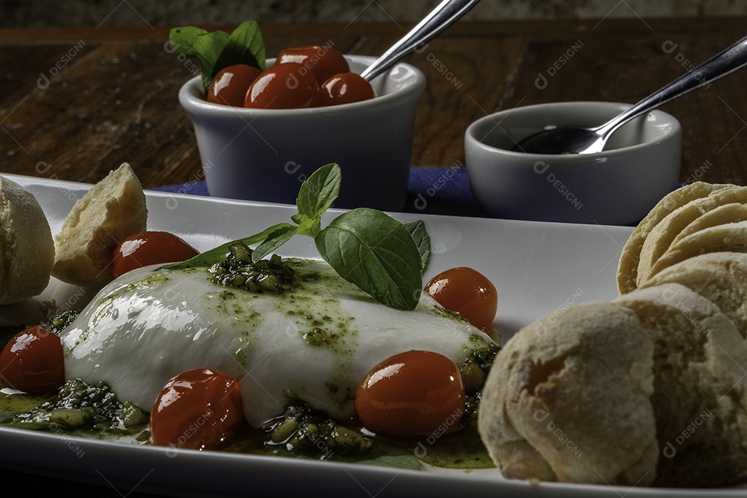 Burrata servida com azeite virgem extra, tomate e manjericão com pães em fatias.