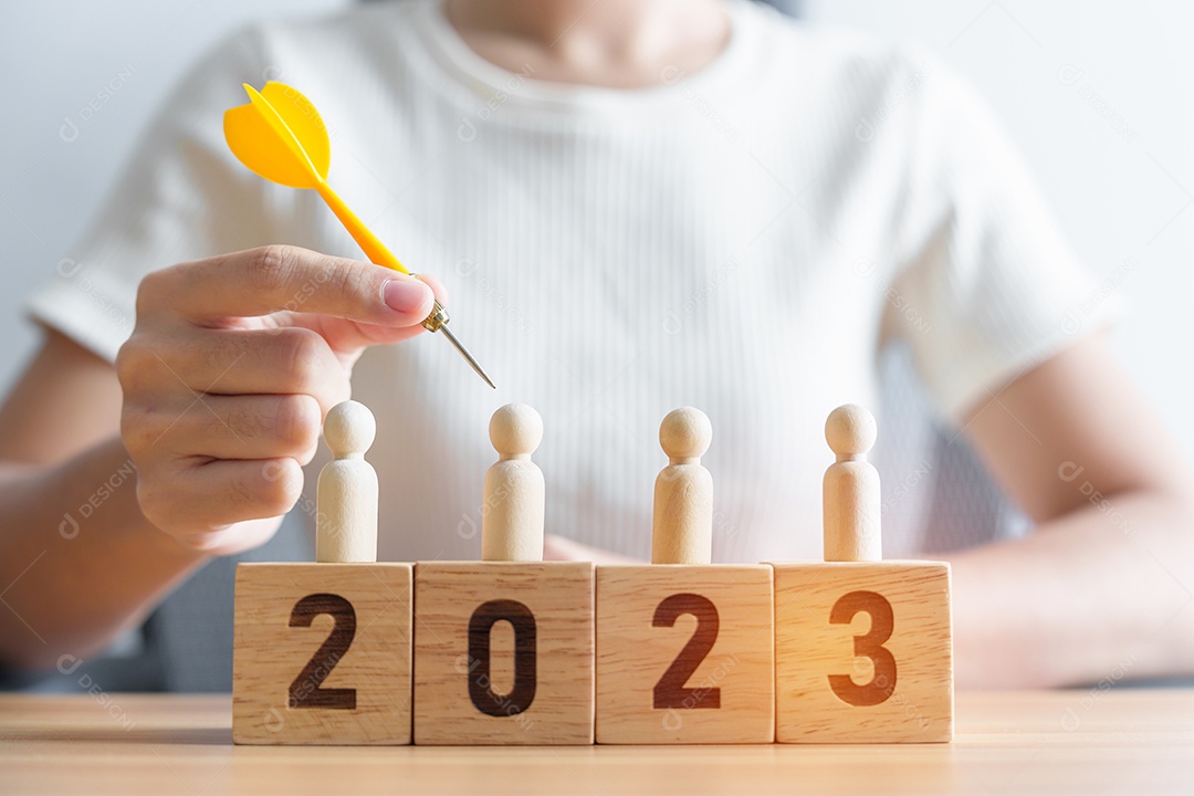 Mão segurando o dardo sobre pessoas e blocos de 2023 anos Objetivo, plano, ação, alvo, estratégia, liderança, Ano Novo e conceito de marketing