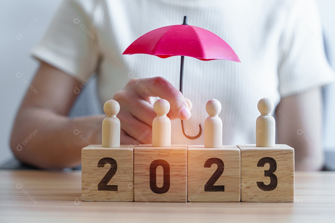 hand holding umbrella cover wooden man staffs with 2023 year block. Insurance, protection, people, human resource management, leadership and new year concepts