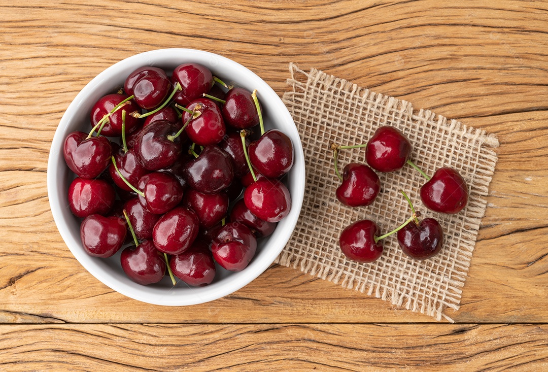 Cerejas vermelhas em uma tigela sobre a mesa de madeira.