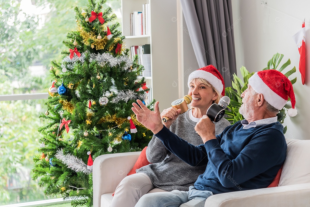 Casal de idosos senta-se no sofá da sala e canta juntos no dia de natal.