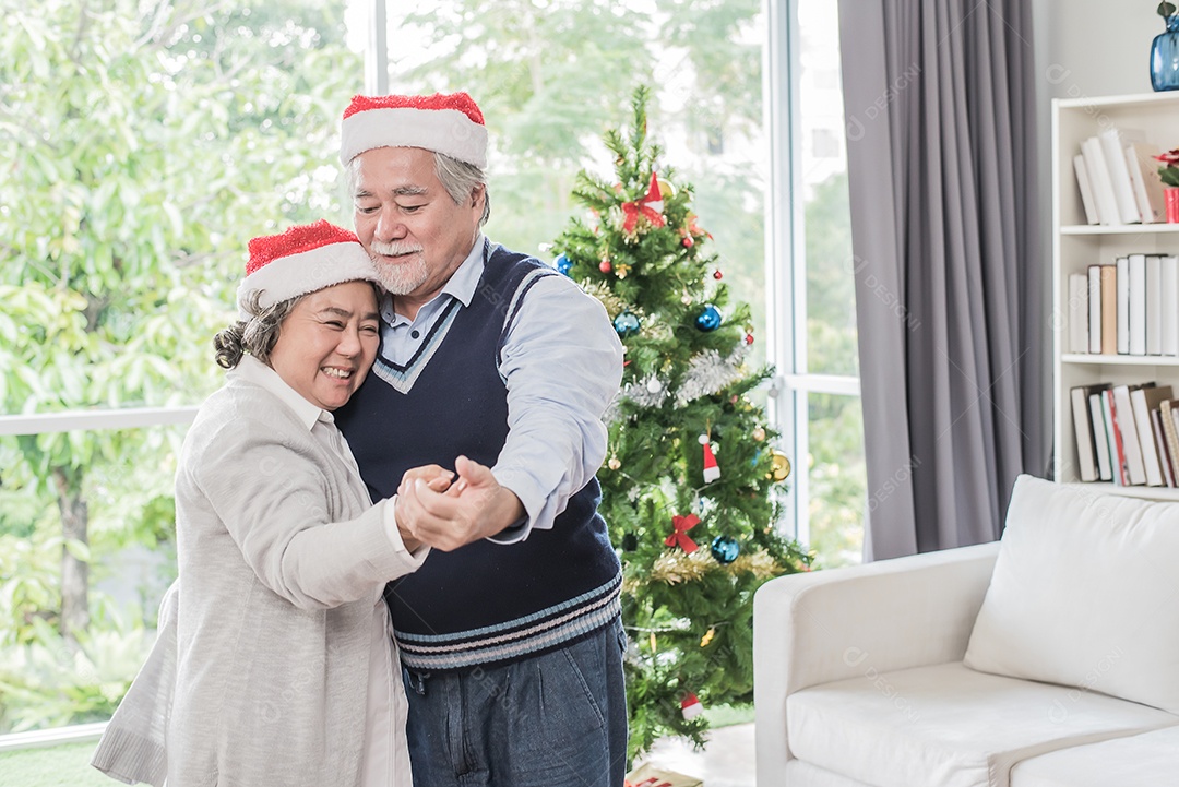Casal idosos, marido e mulher usando chapéus de natal e dançando, árvore de fundo.