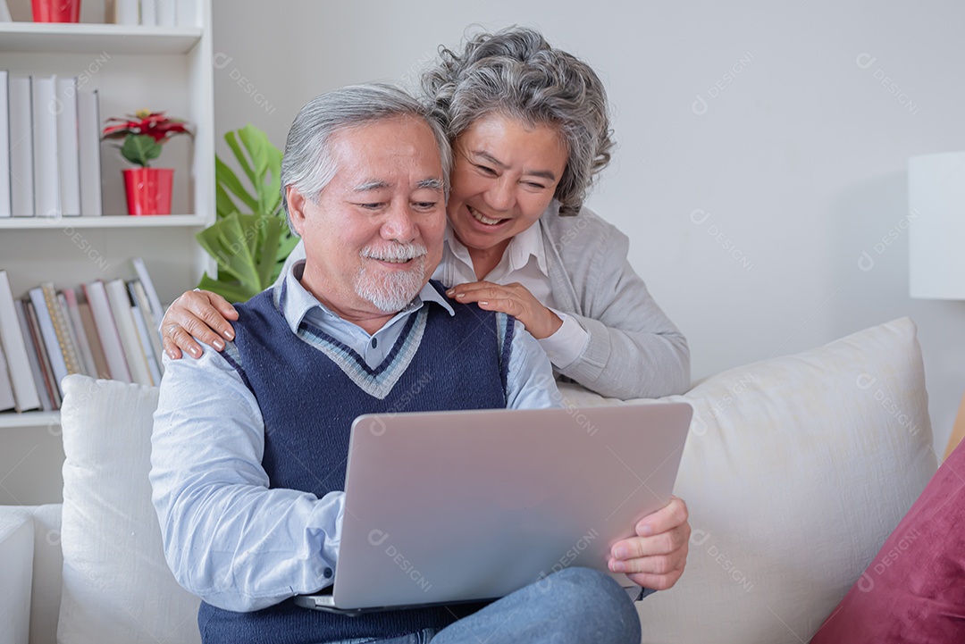 Marido e mulher sênior sentam no sofá olham para o notebook do computador