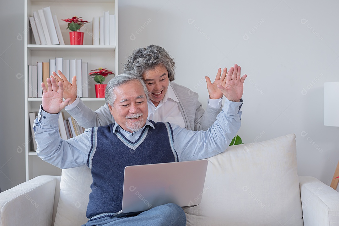 Marido e mulher sênior sentam no sofá olham para o notebook do computador