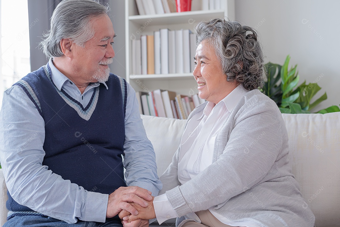 Marido sênior, segurando a mão de sua esposa, sente-se alegremente no sofá