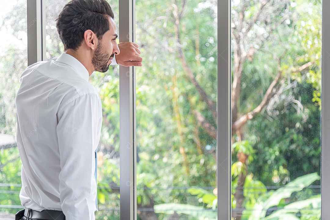 Empresário em pé contemplando olhar para fora do escritório